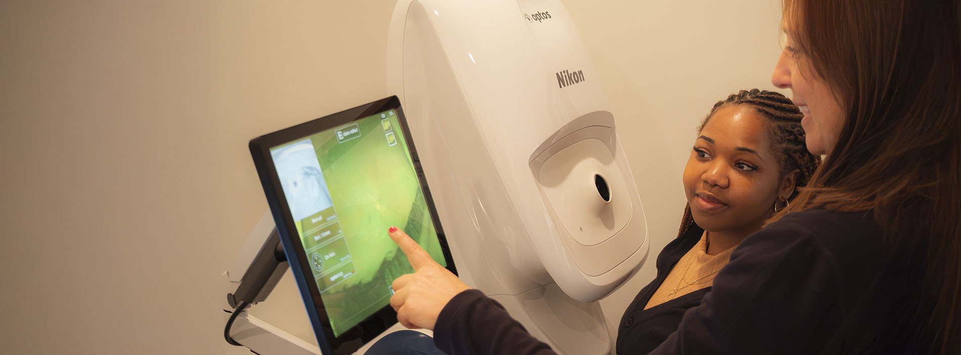 A person interacting with an electronic device, possibly a medical machine, in a room with a woman standing nearby.