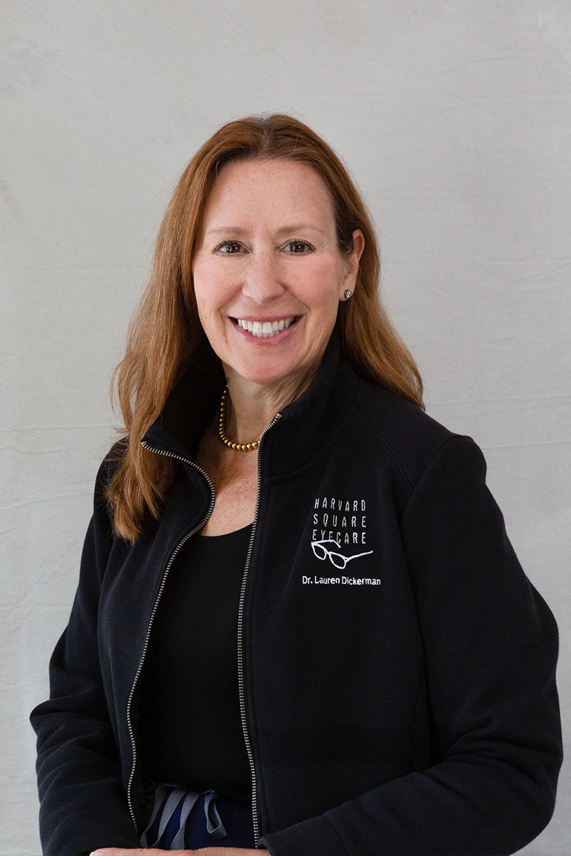 A smiling woman wearing a black jacket with a white logo on her chest, posing for a portrait with a confident expression.