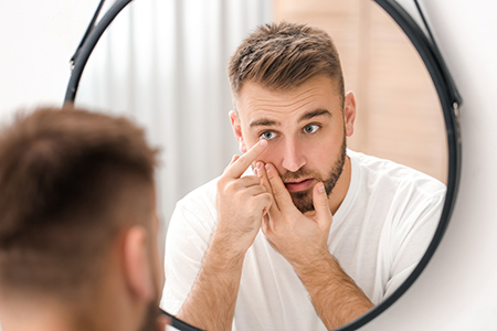 A man with short hair is seen looking into a mirror while preparing his skin with a handheld device.
